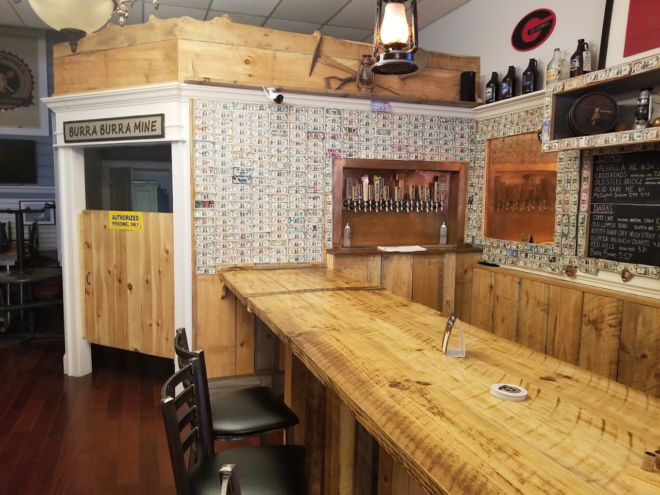 Bar with wooden counter, beer taps, and rustic decor. Two chairs are in front of the counter.