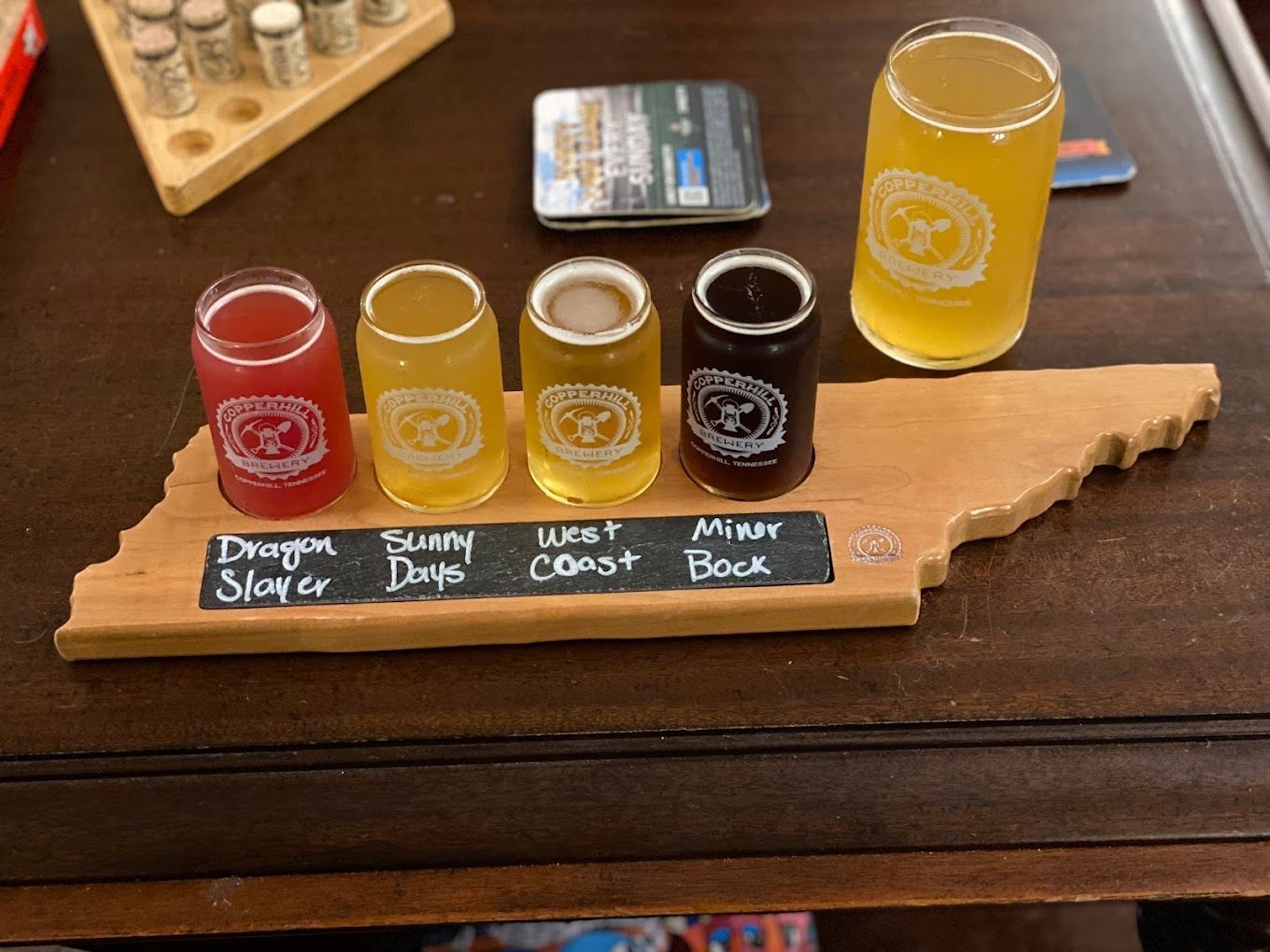 Beer flight in Tennessee-shaped wooden tray with five small glasses, plus a full glass, on a wooden table.