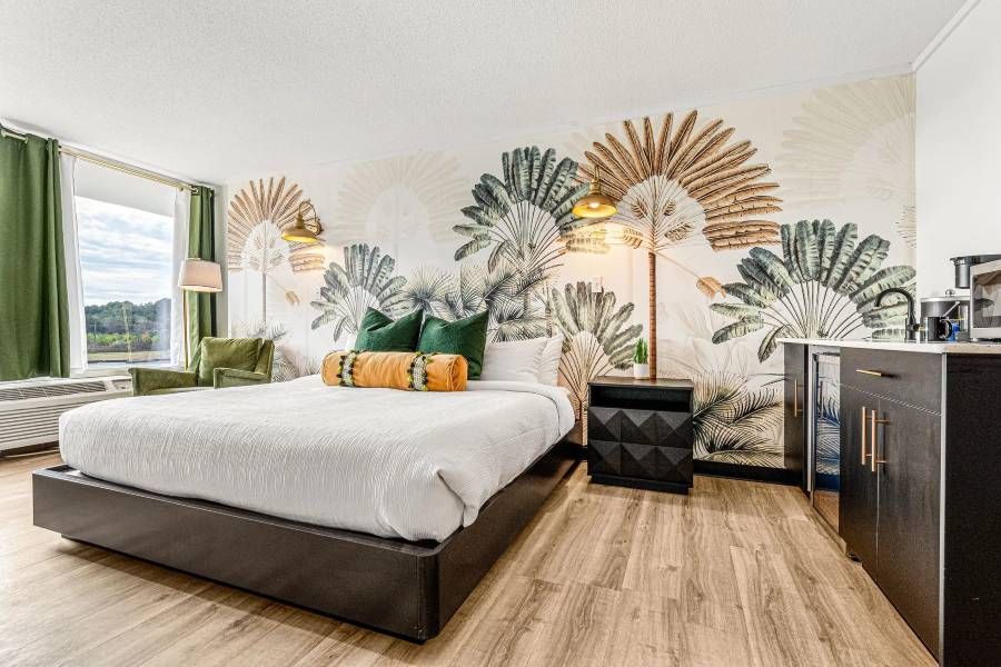 Hotel room with a king bed, tropical mural, wood floors, and dark accents.