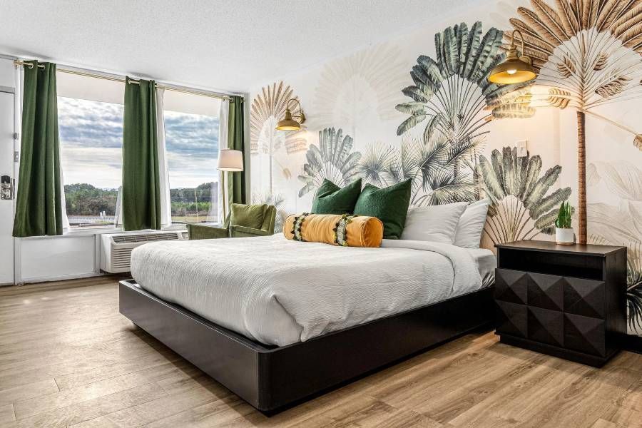 Hotel room with king bed, botanical mural, green accents, and outdoor view.