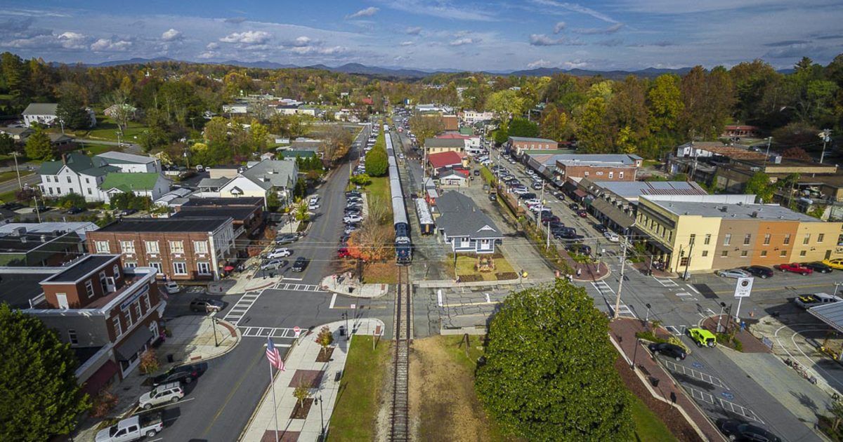 Aerial view of a town with train tracks running through the center; buildings, cars, trees, and people.