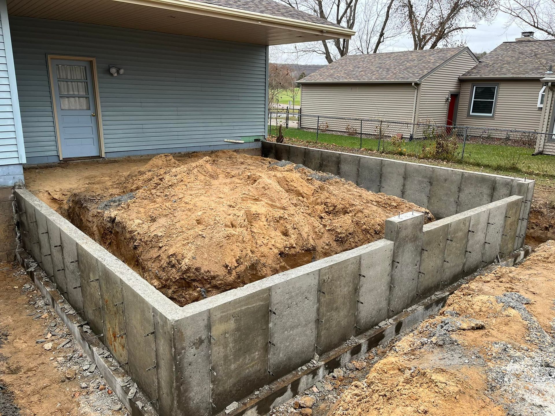Picture of the preparation of making a frost wall in Wisconsin around a house. You can see the concrete slabs being dug into the ground creating a frostline. 
