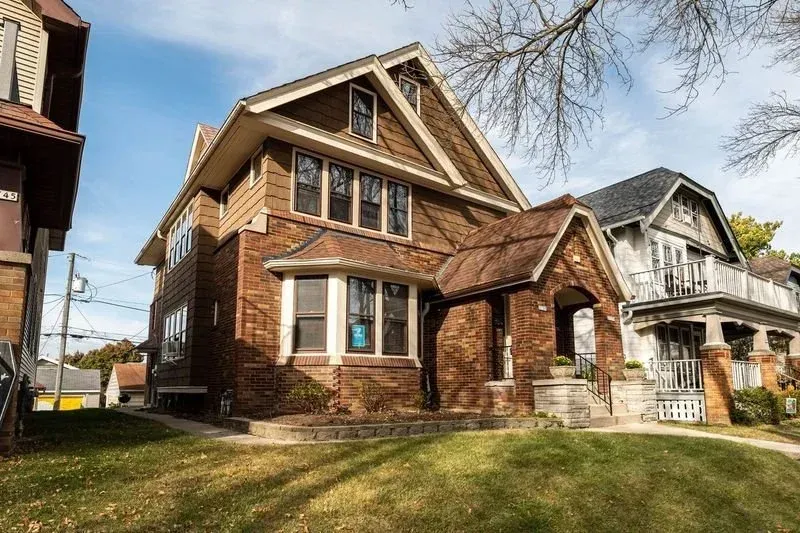 Brick house with gabled roof and front porch on a grassy residential street.