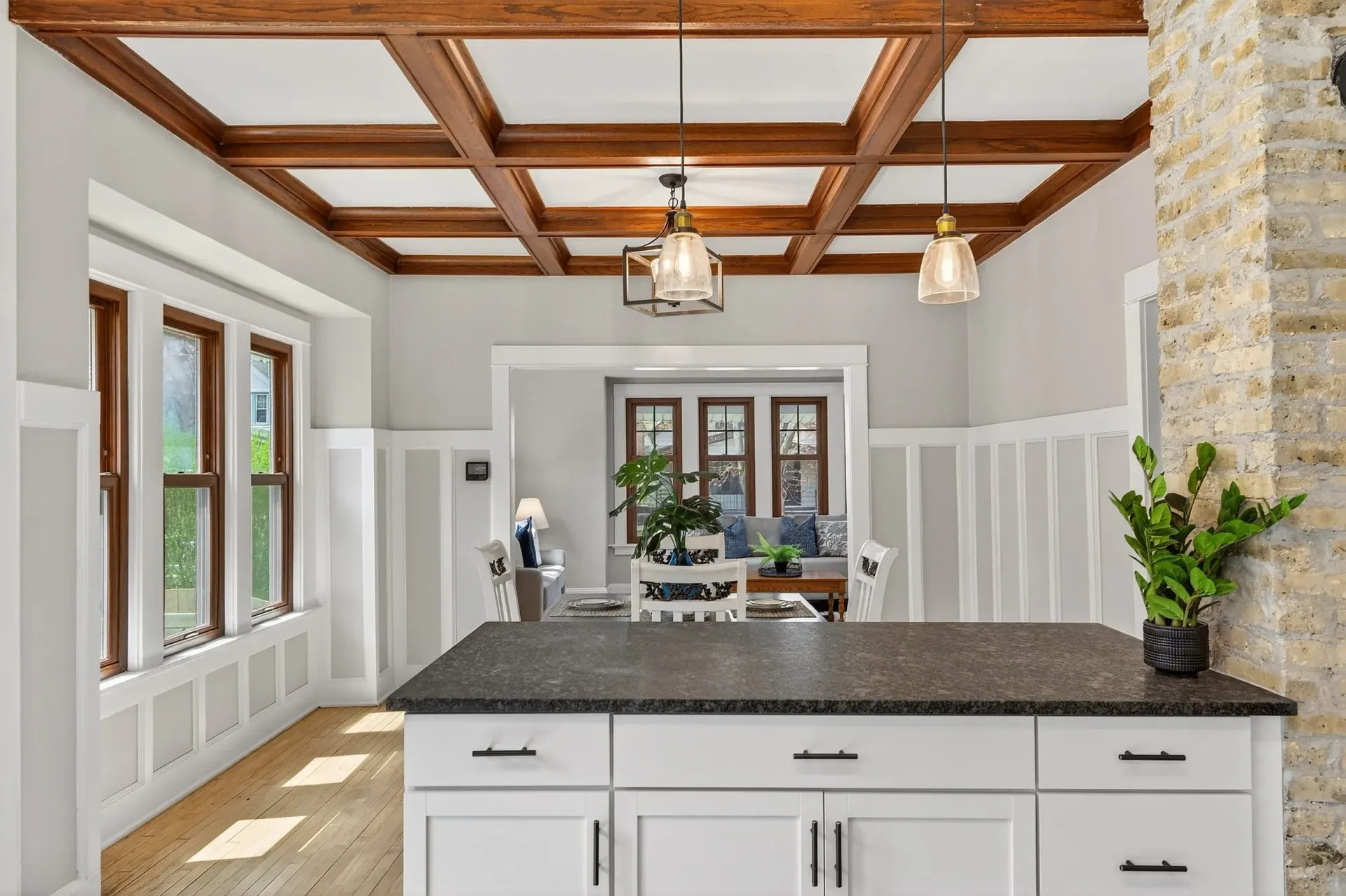 Modern kitchen with white cabinets, dark island countertop, wood beam ceiling, and a stone fireplace.