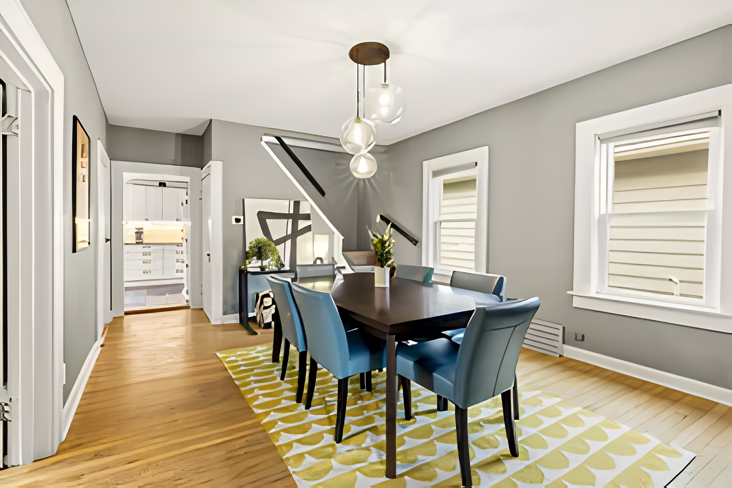 Bright dining room with a dark table, blue chairs, gray walls, and yellow patterned rug