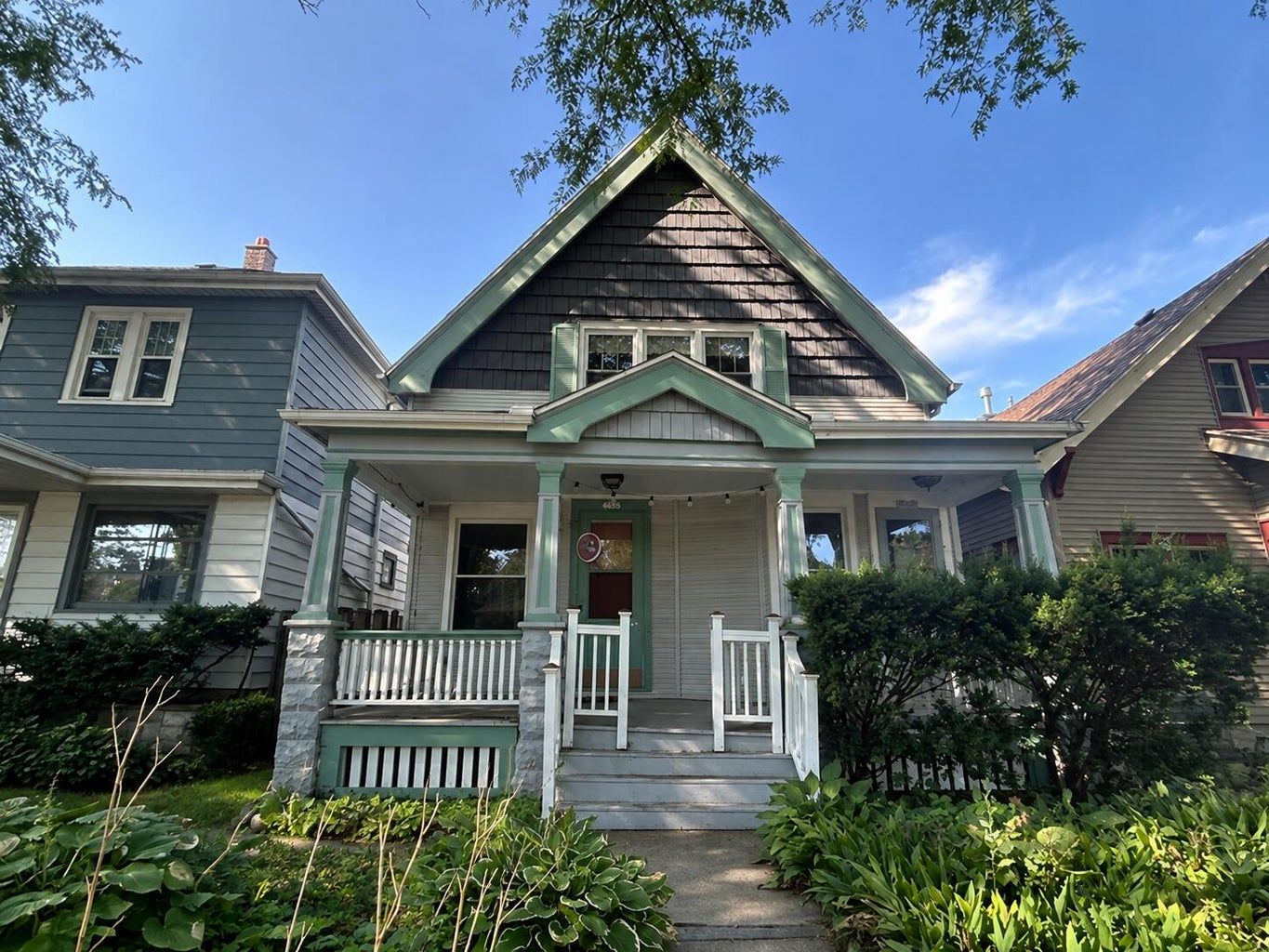 A gray Victorian house with a front porch, green trim, and steps leading to the entrance.