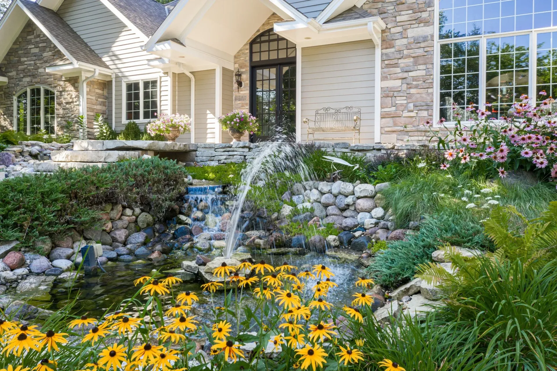 House with wraparound white porch and landscaped garden on a sunny day
