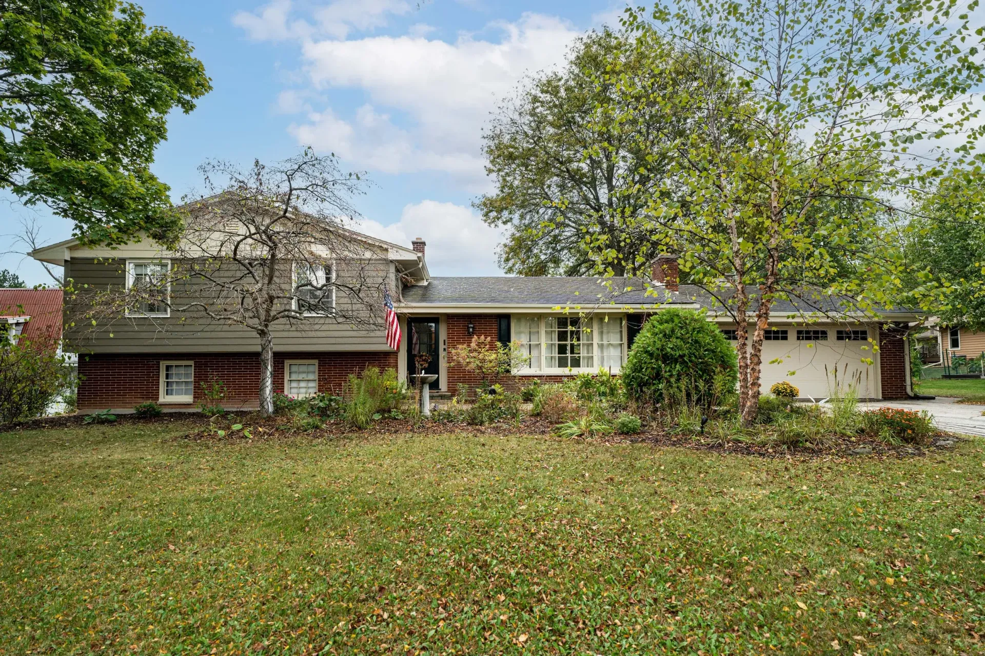 Single-story brick house with a large front lawn and trees under a cloudy sky