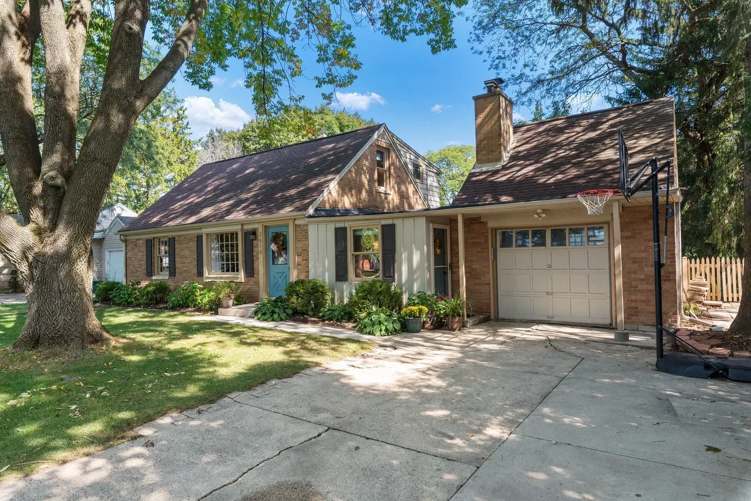 Single-story brick house with a garage, front porch, and large trees shading the driveway