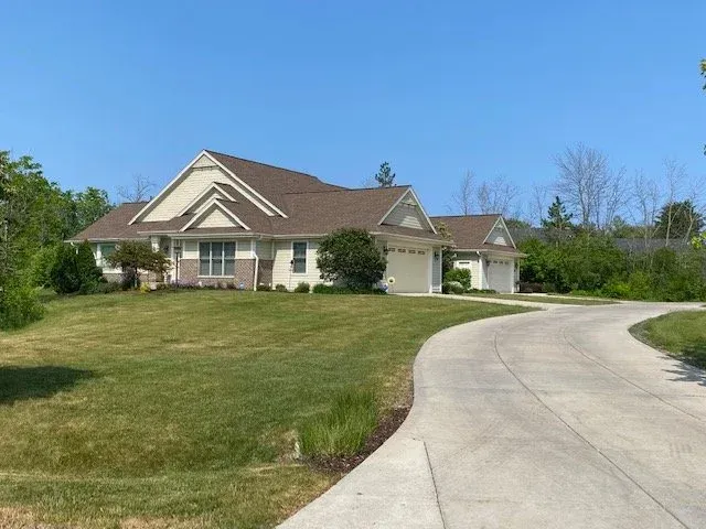 Suburban house with tan roof and curved driveway beside a large green lawn under a blue sky