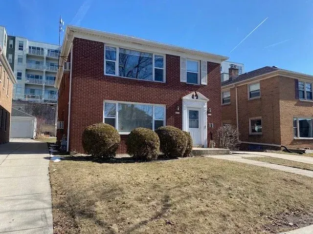 Brick two-story house with white trim and front shrubs on a sunny day
