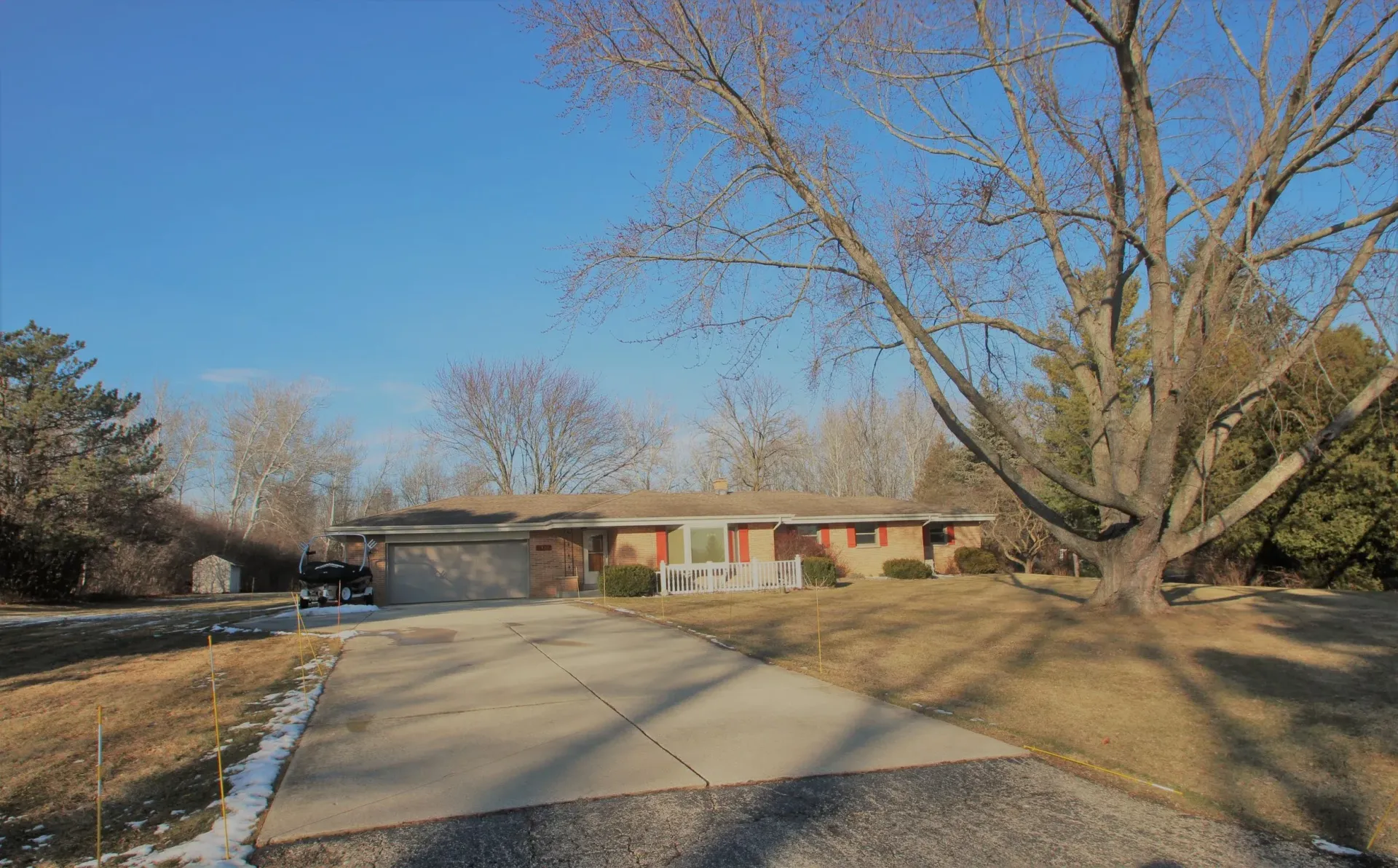Quiet suburban street leading to a single-story brick house under a clear blue sky.