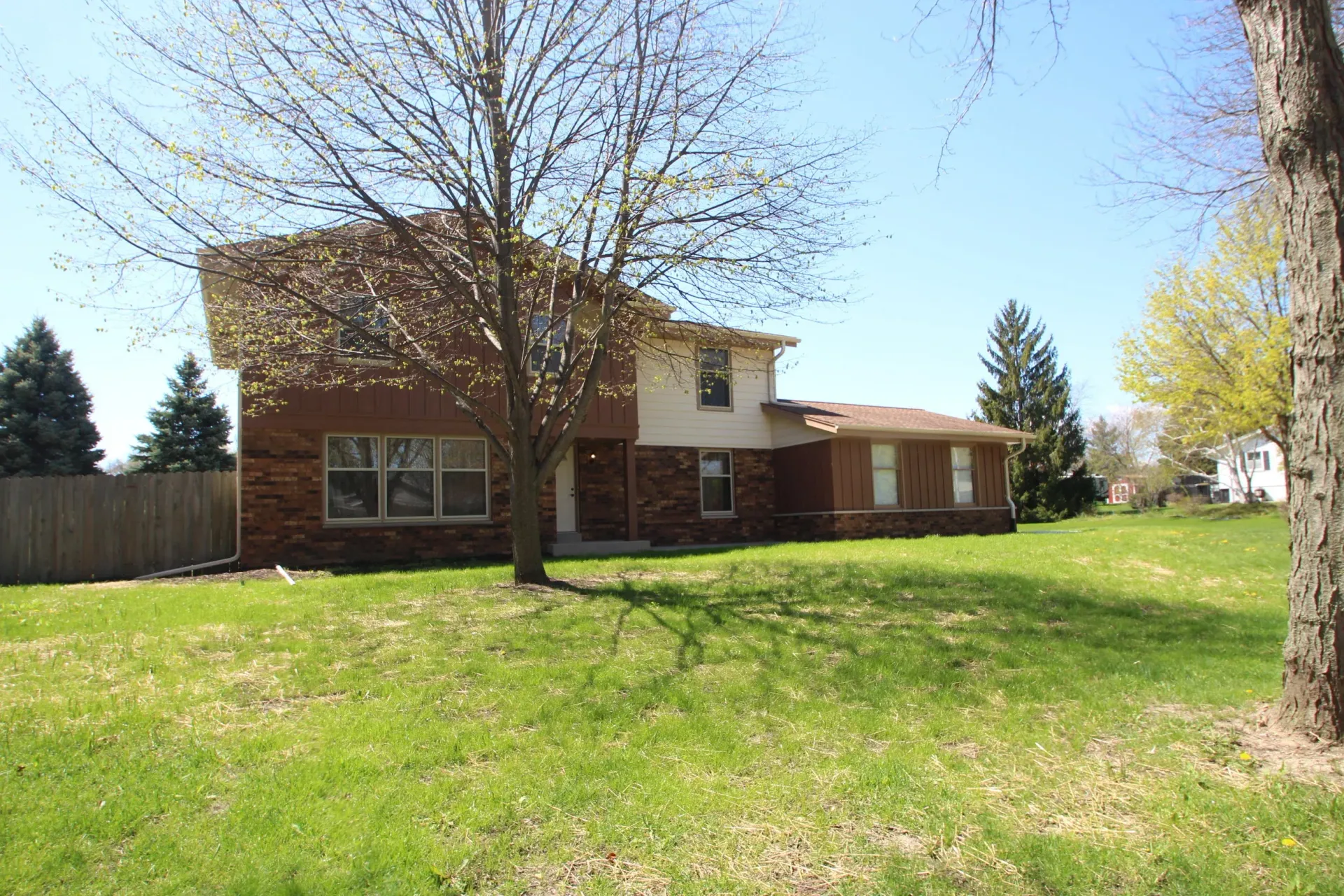 Two-story brick house with a large green lawn and leafless tree in front