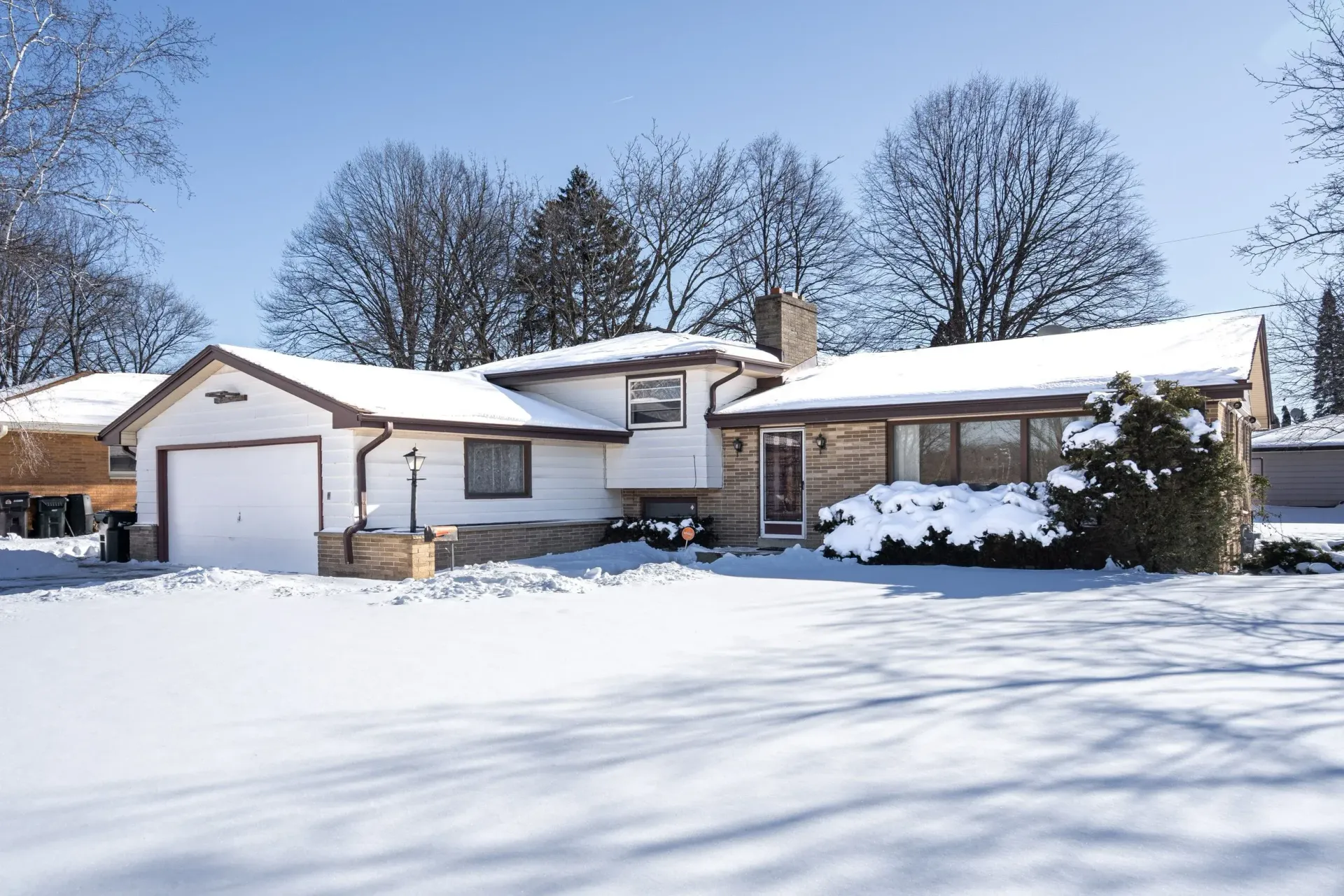 Snow-covered suburban house with garage and bare trees in a winter landscape