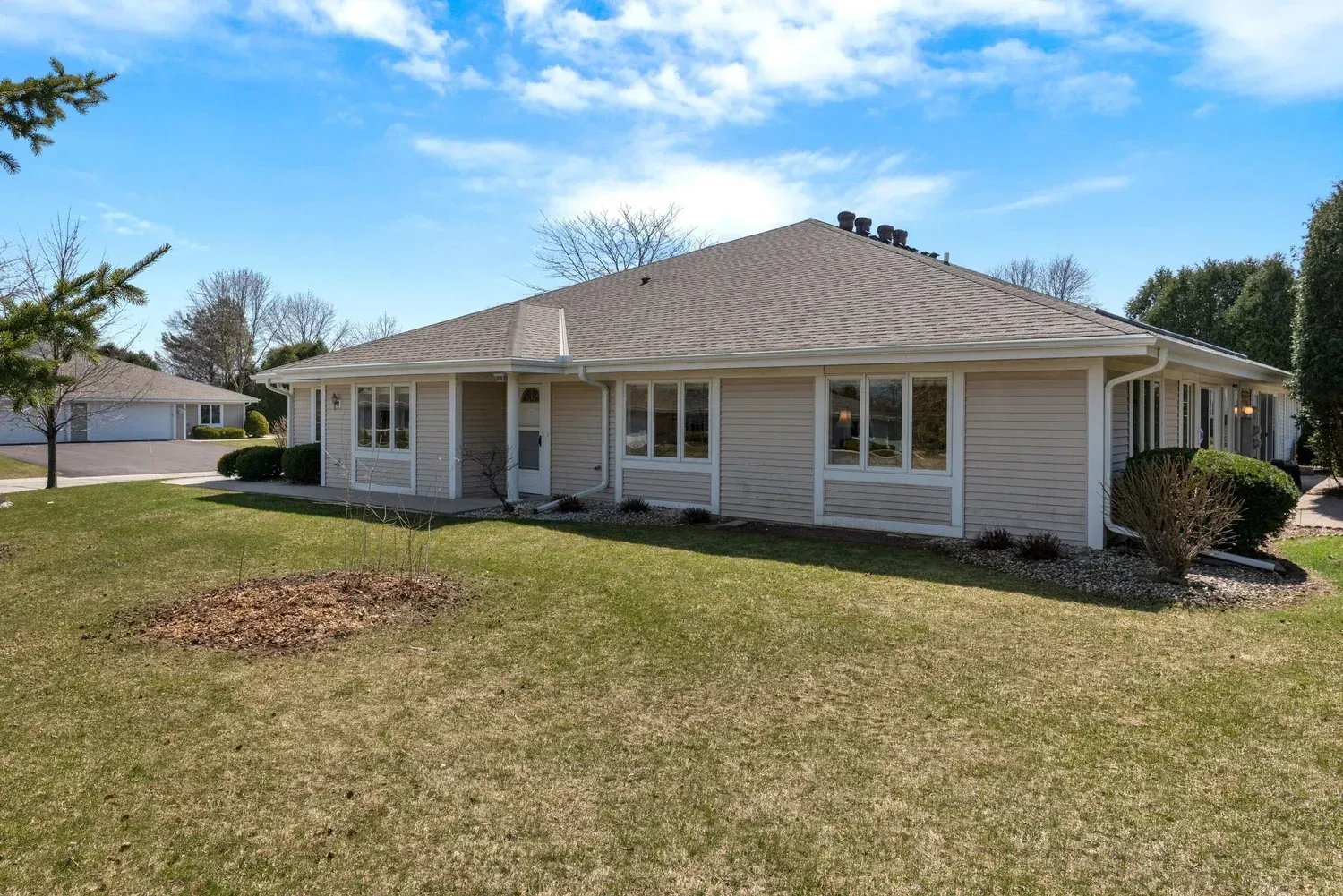 Single-story beige house with white trim and a large front lawn under a clear blue sky