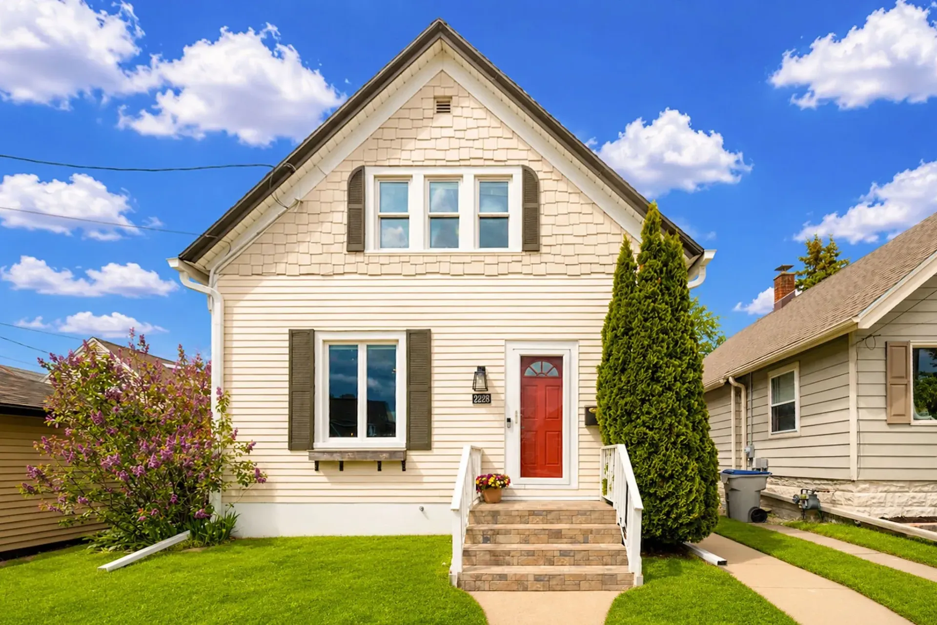 White two-story house with red front door, front steps, green lawn, and blue sky with clouds