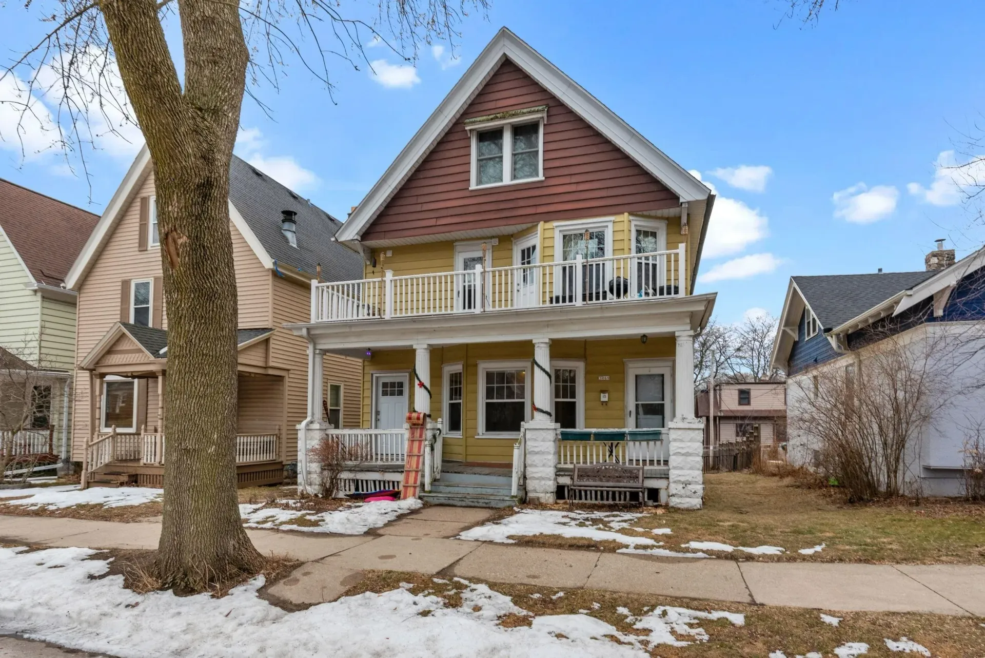 Suburban house with a front porch, balcony, and light snow on the yard and roof