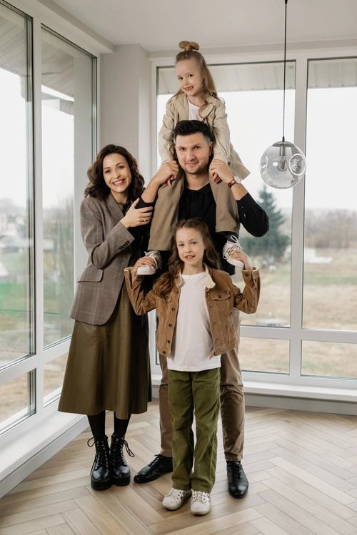Family of four standing together in a bright room, with two children sitting on their parents' shoulders.