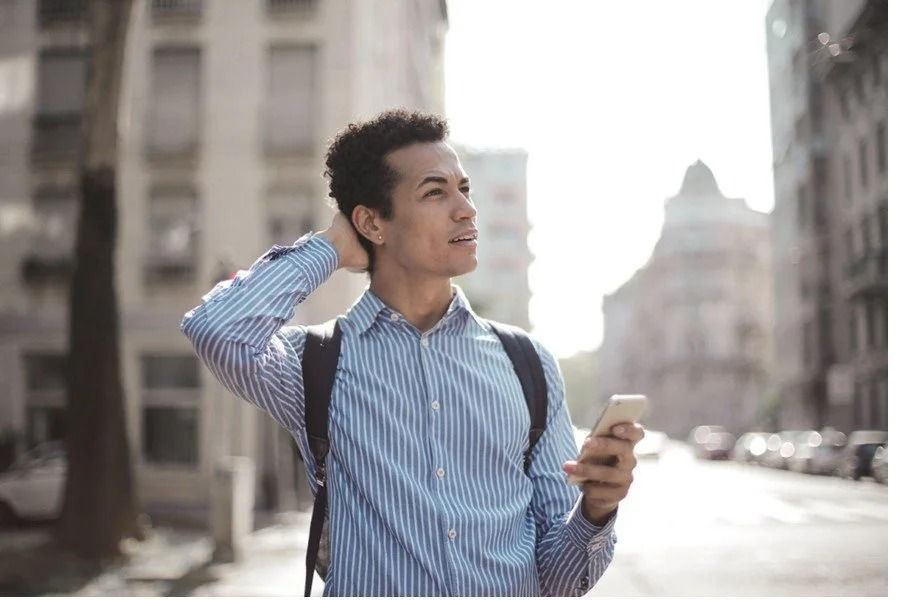 Man holding a phone and backpack on a city street, looking off to the side.