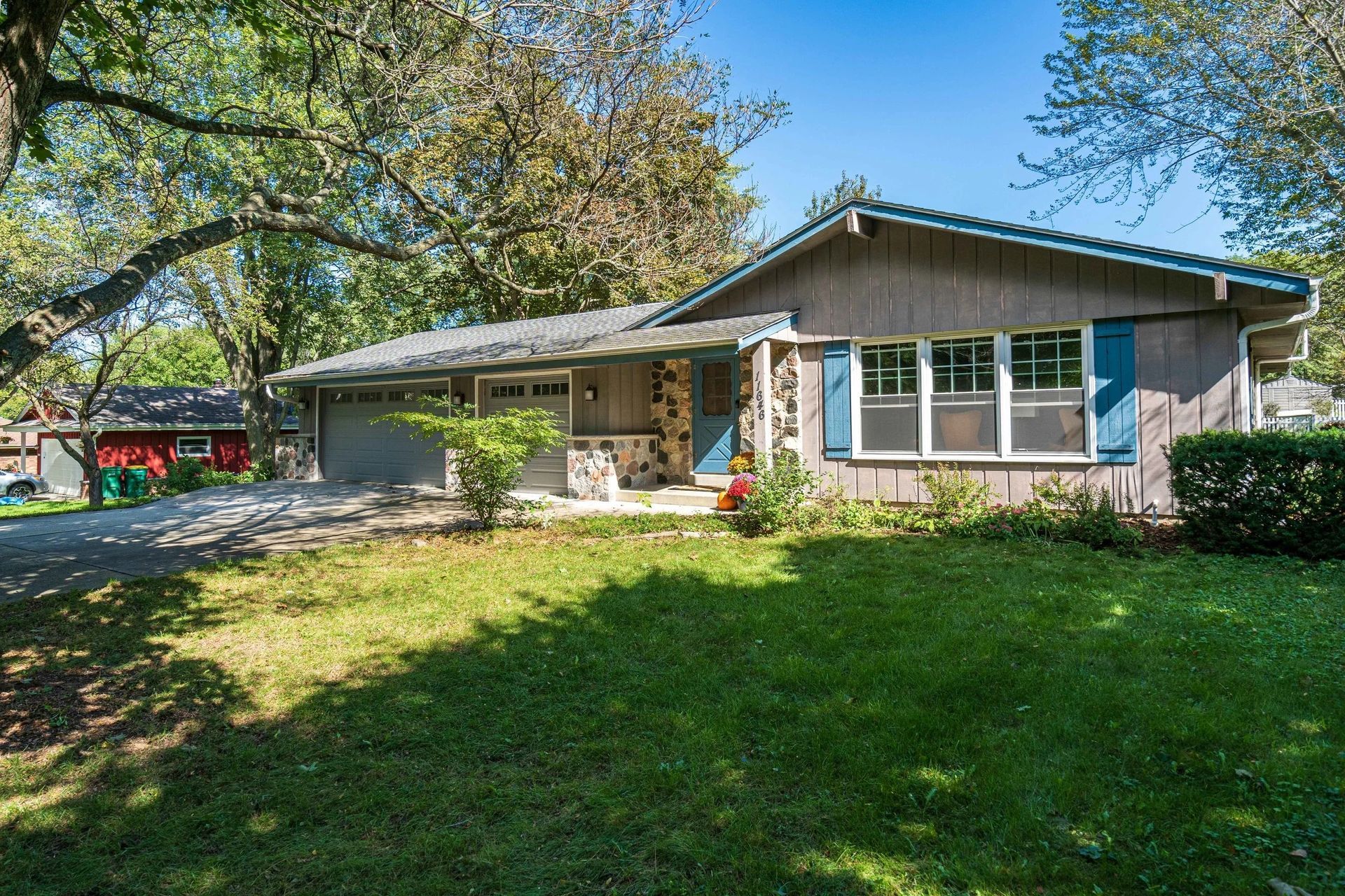 Single-story house with a stone porch, large green lawn, and trees in the yard