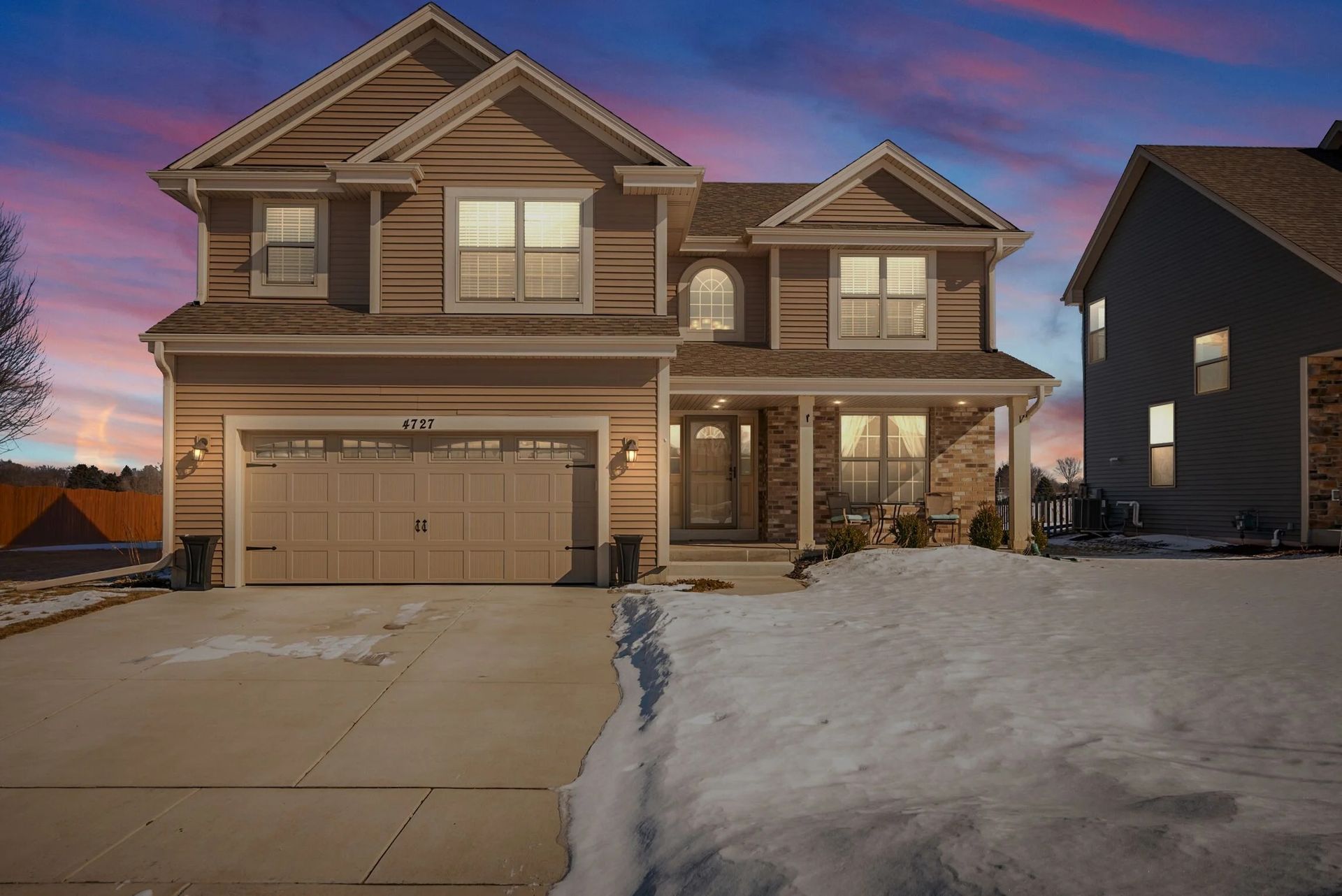 Two-story suburban house with garage and snow-covered driveway at sunset