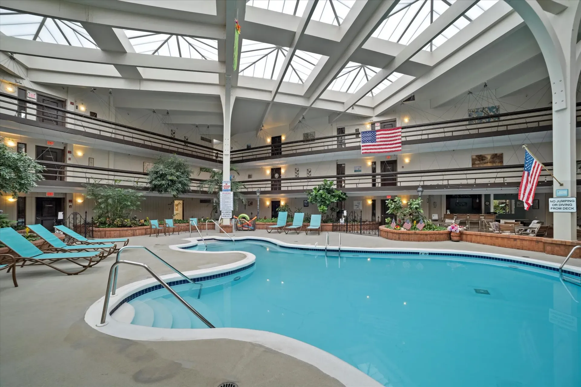 Indoor hotel pool with skylit atrium, lounge chairs, and American flags