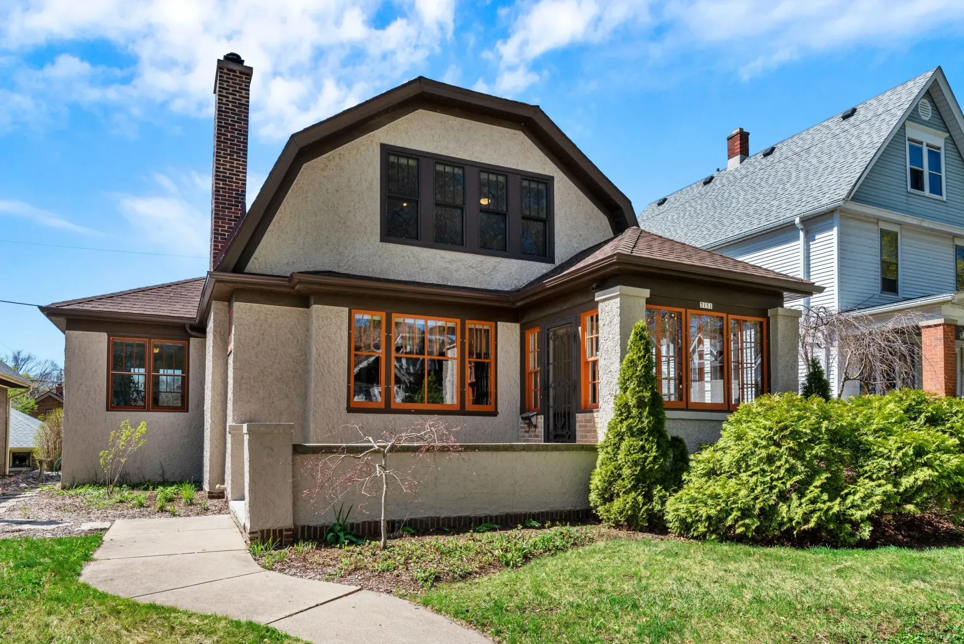 A beige stucco house with dark trim, wood-framed windows, and a front lawn on a sunny day