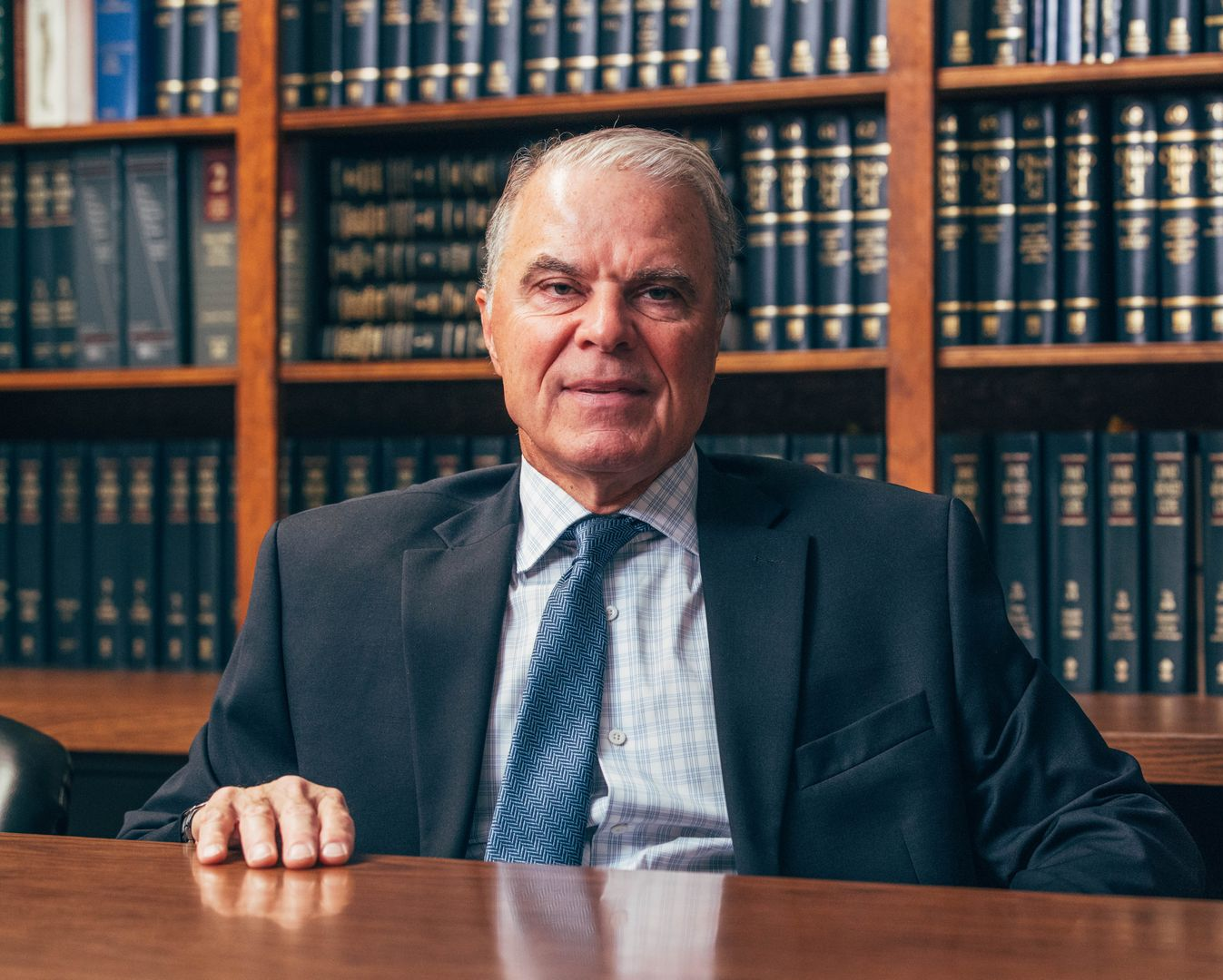 Man in a suit smiles in front of a law library with dark book shelves.
