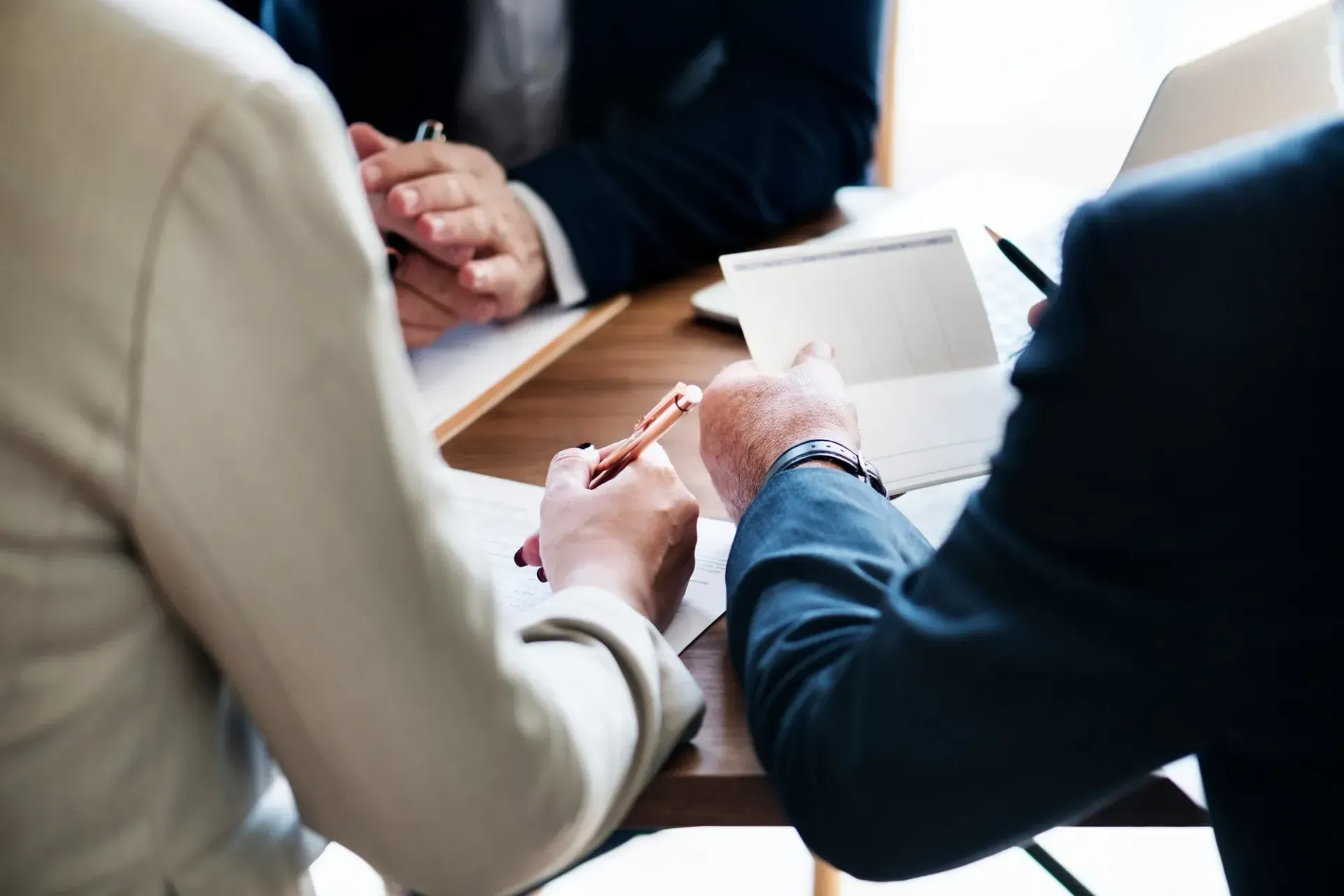 People in business attire at a table, discussing documents. One person points, another writes.