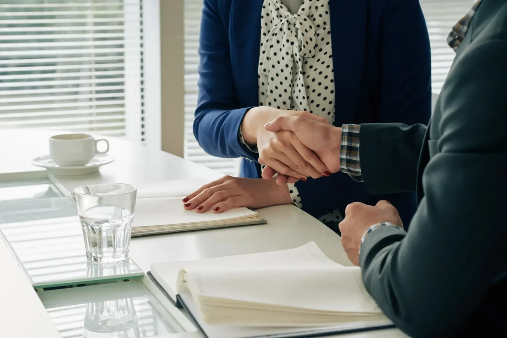 Two people shaking hands over a desk in an office setting.