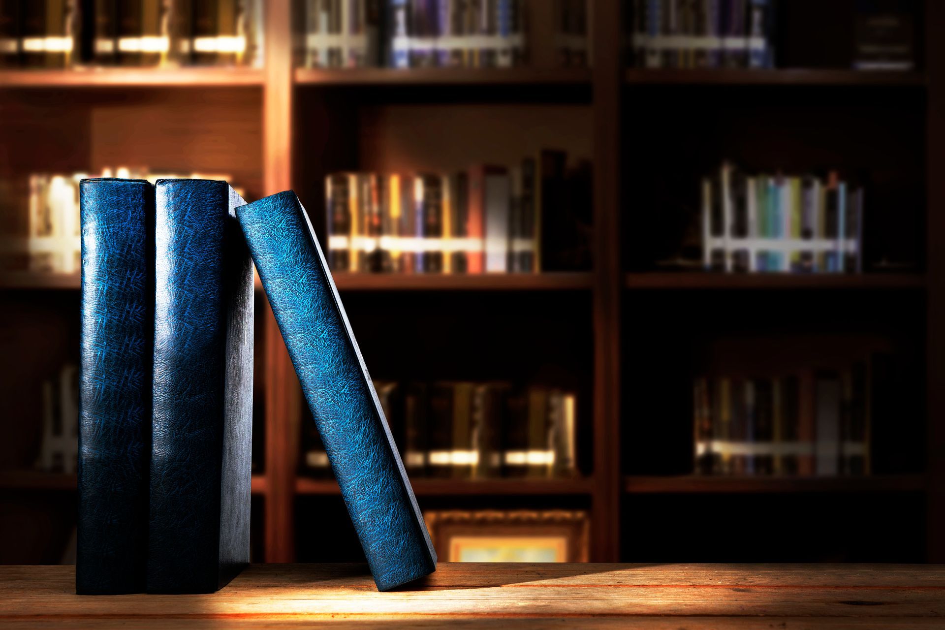 Books on a wooden surface in front of a bookcase, dark lighting.