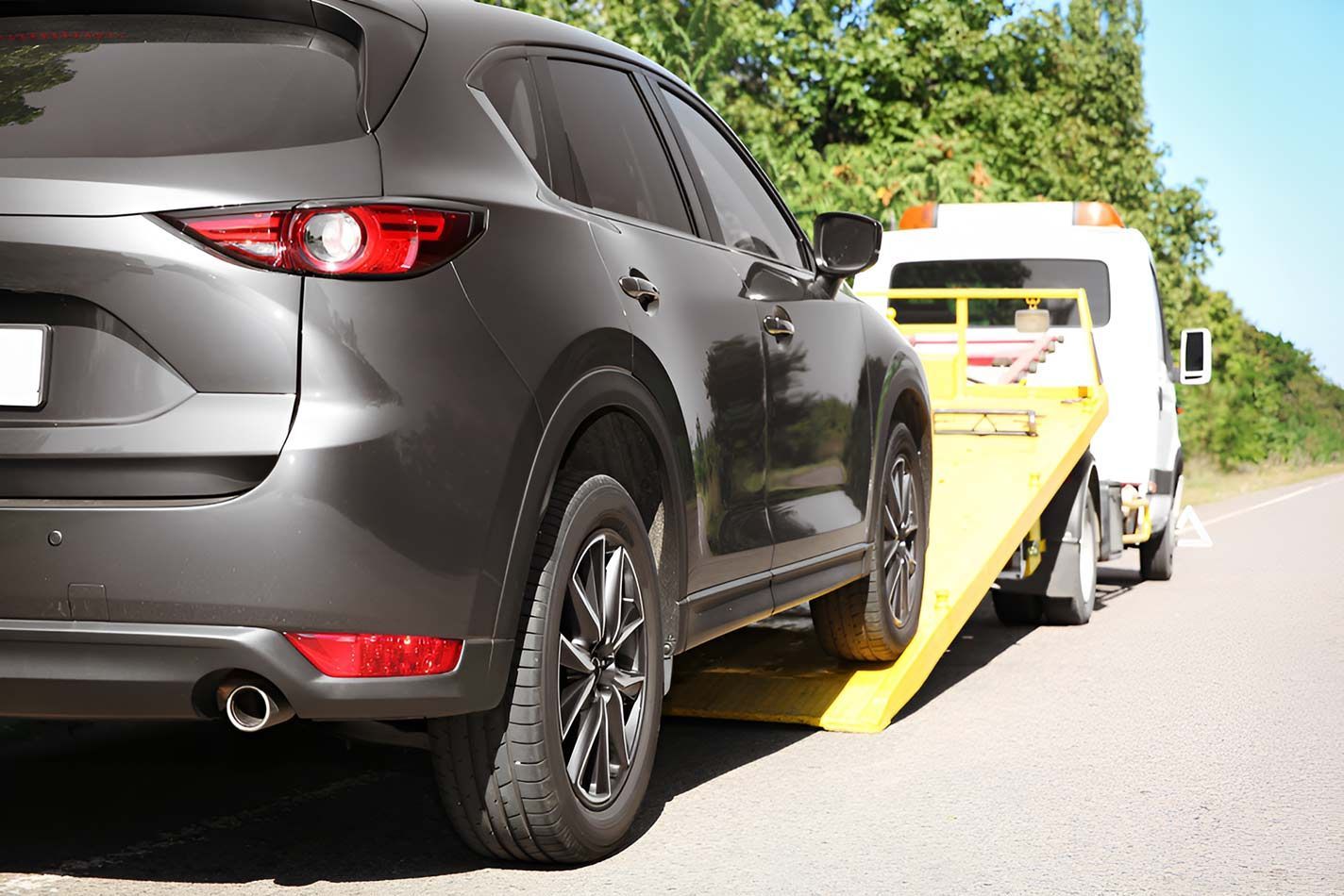 A Car Is Being Towed By A Tow Truck On The Side Of The Road — Milini's Panel, Paint & Towing in Tully, QLD