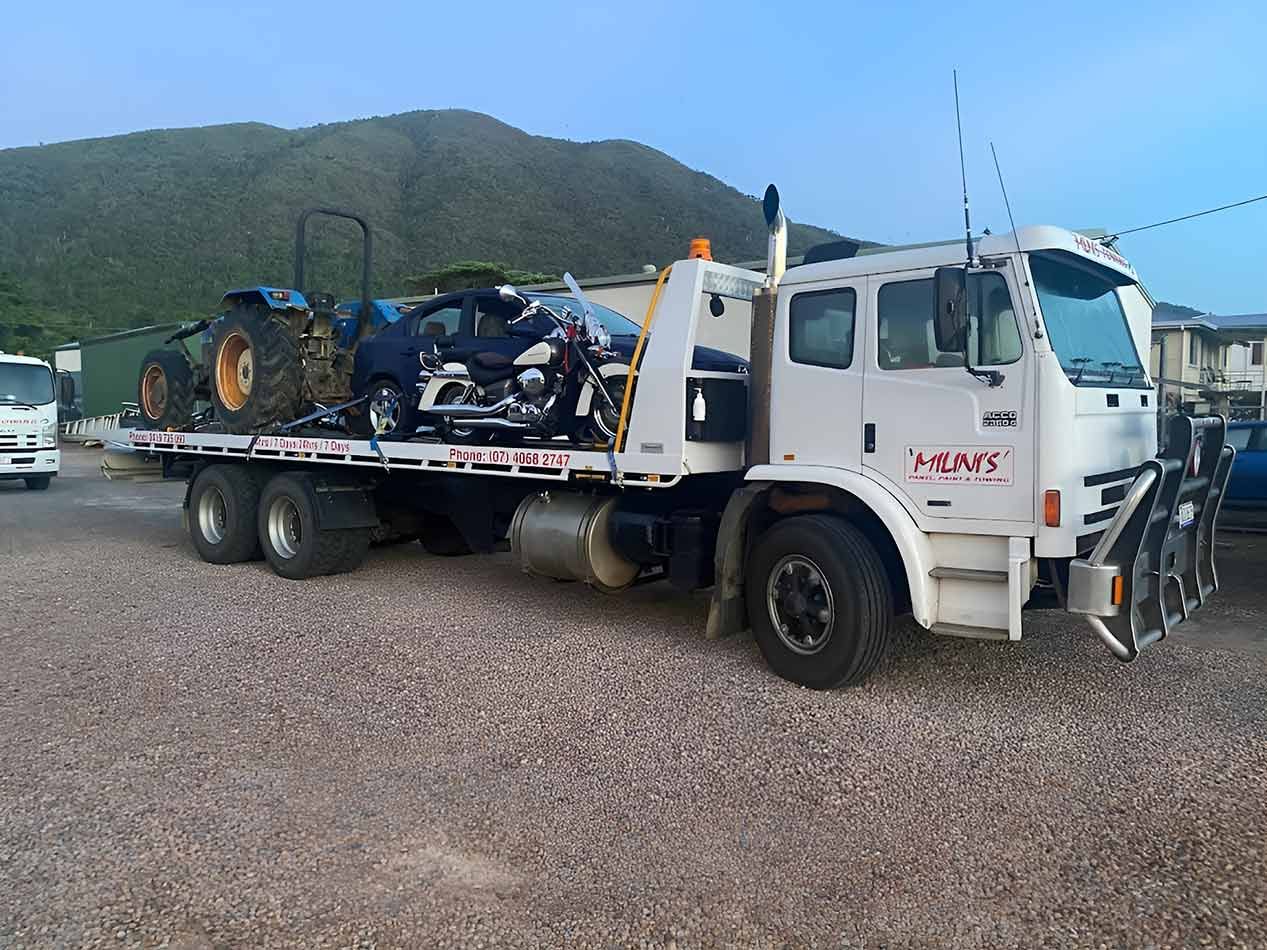 A Tow Truck Is Carrying A Tractor And A Motorcycle On Its Flatbed — Milini's Panel, Paint & Towing in Tully, QLD