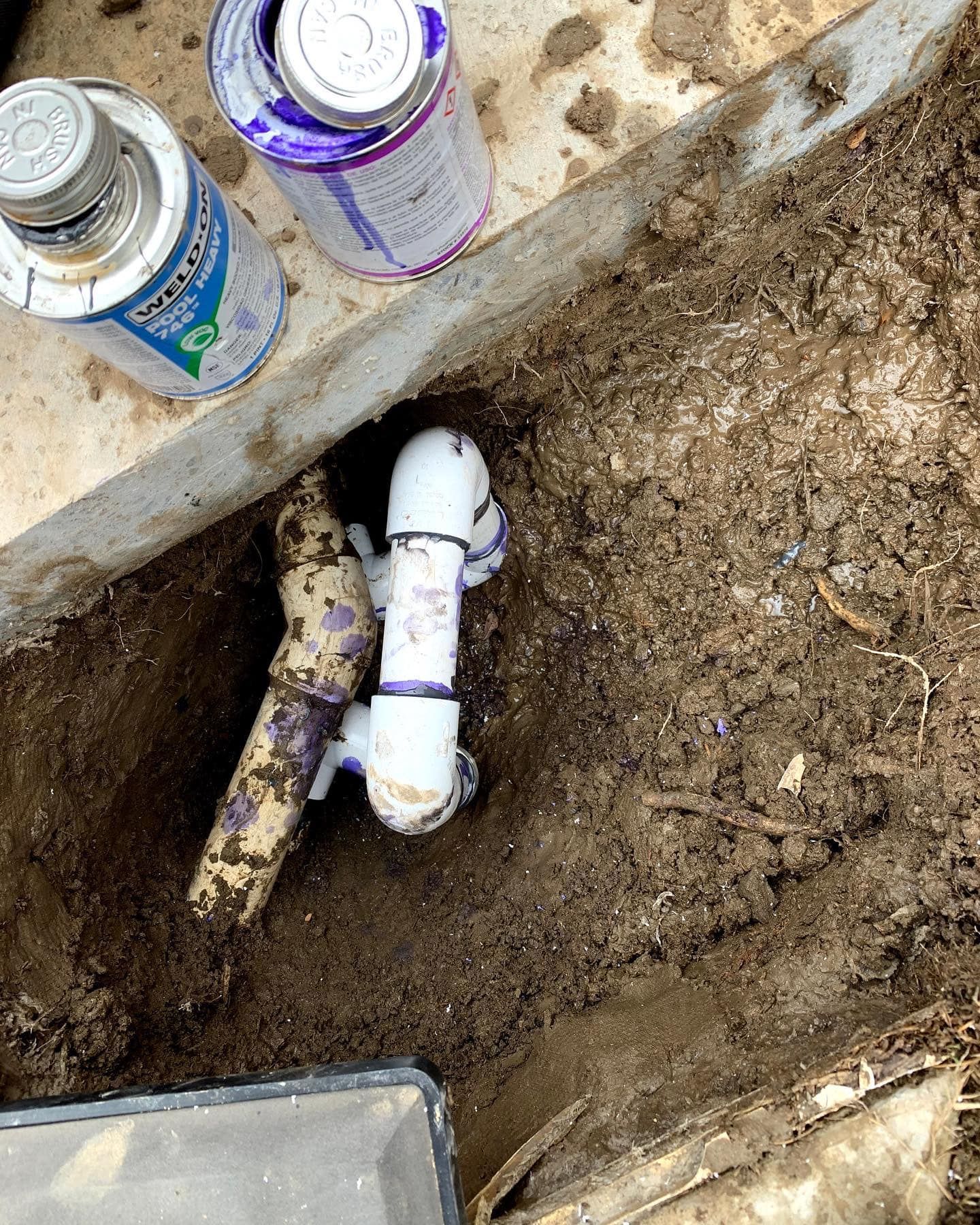 a white pipe is laying in the dirt next to two bottles of sealant