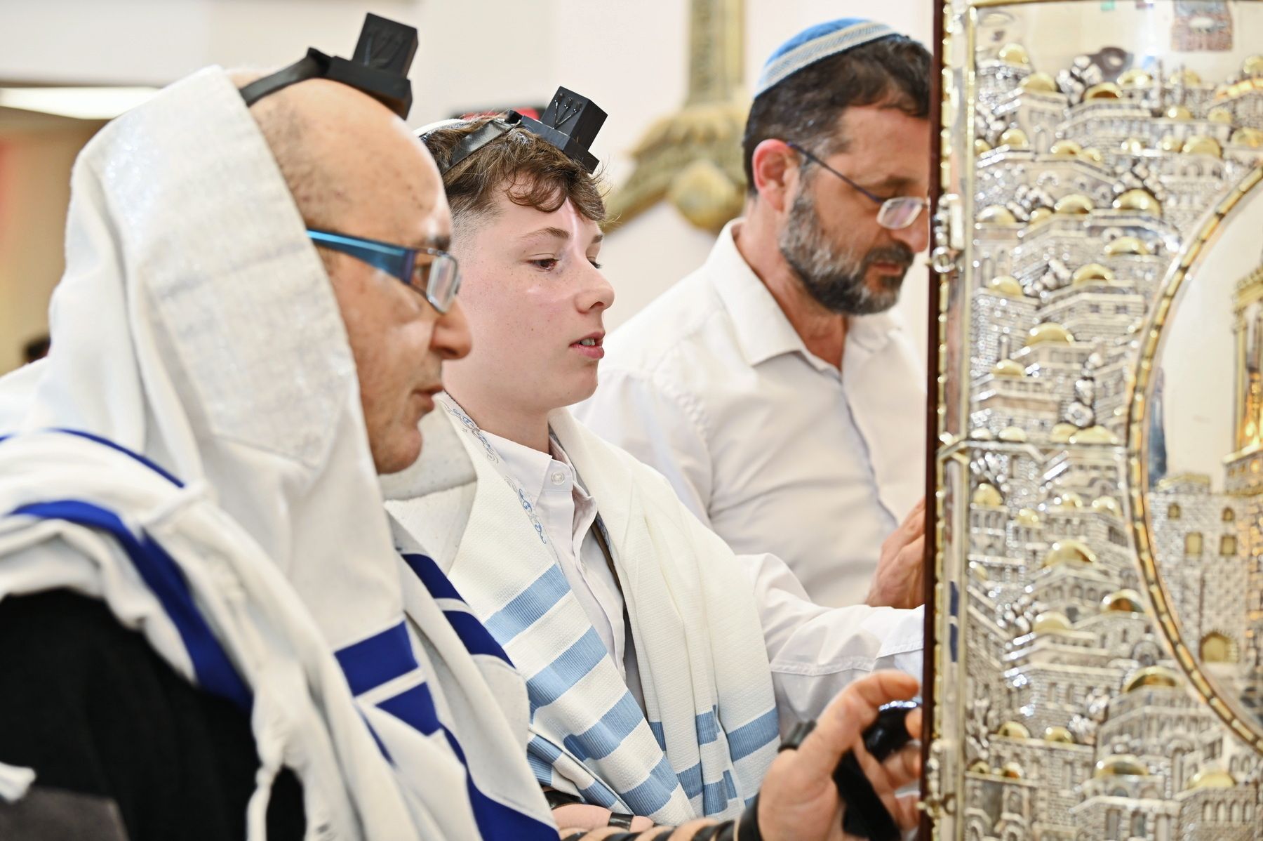 אנשים עוטים טליתות ותפילין ומתפללים לצד ארון קודש מקושט