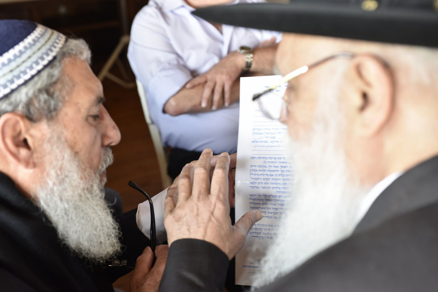 שני גברים מזוקנים משוחחים, ואחד מהם מחזיק מסמך, בסצנה פנימית בתקריב.
