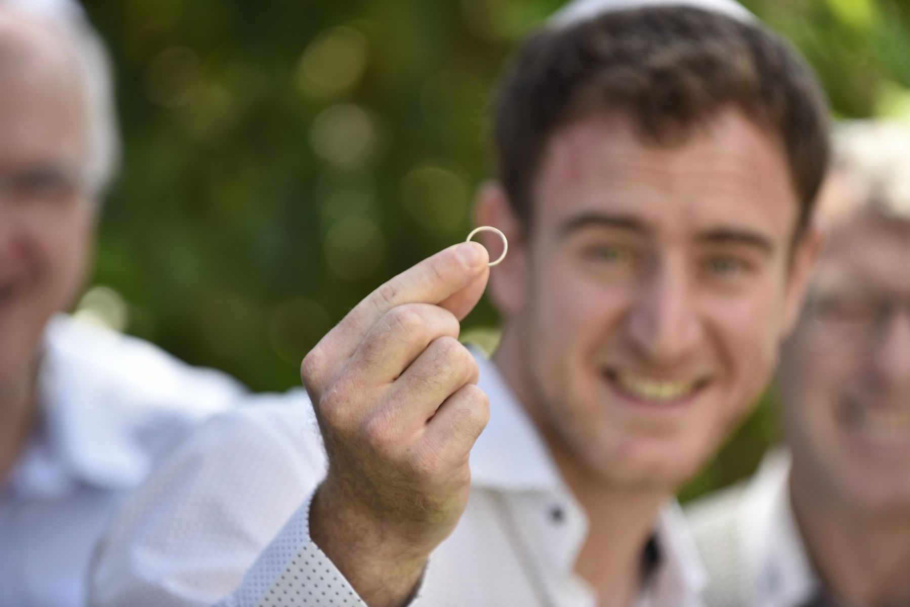 גבר מרים טבעת נישואין באוויר בחוץ, וברקע גבר מחייך ומטושטש