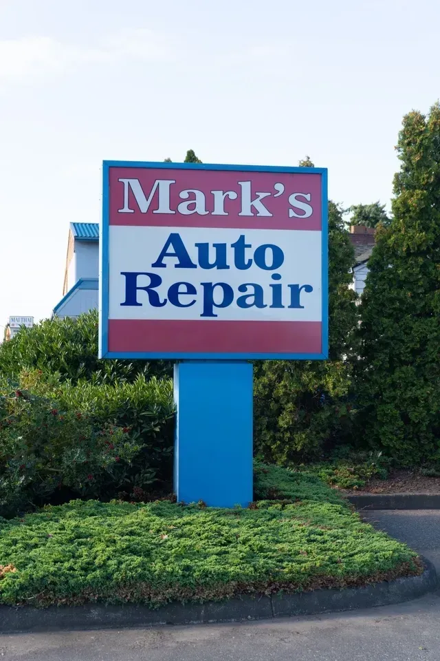 A man wearing a black hat and glasses is working on a car engine | Mark's Auto Repair