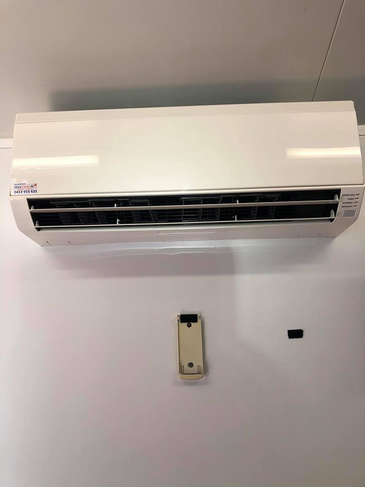 A White Air Conditioner Is Hanging On A White Wall Next To A Remote Control — More Clean Air In Hunter Valley, NSW
