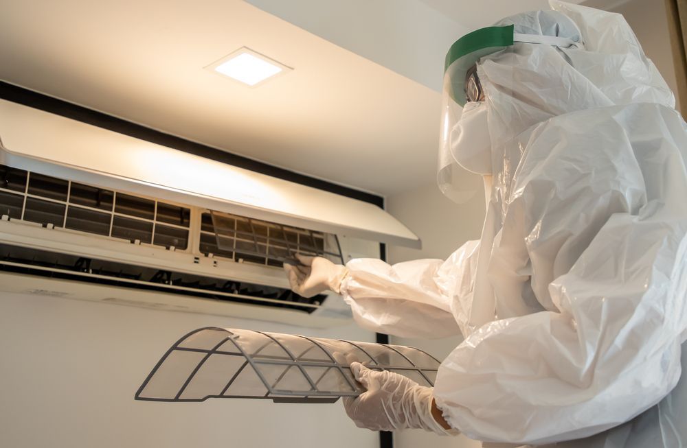 A Man In A Protective Suit Is Cleaning An Air Conditioner — More Clean Air In Morisset, NSW