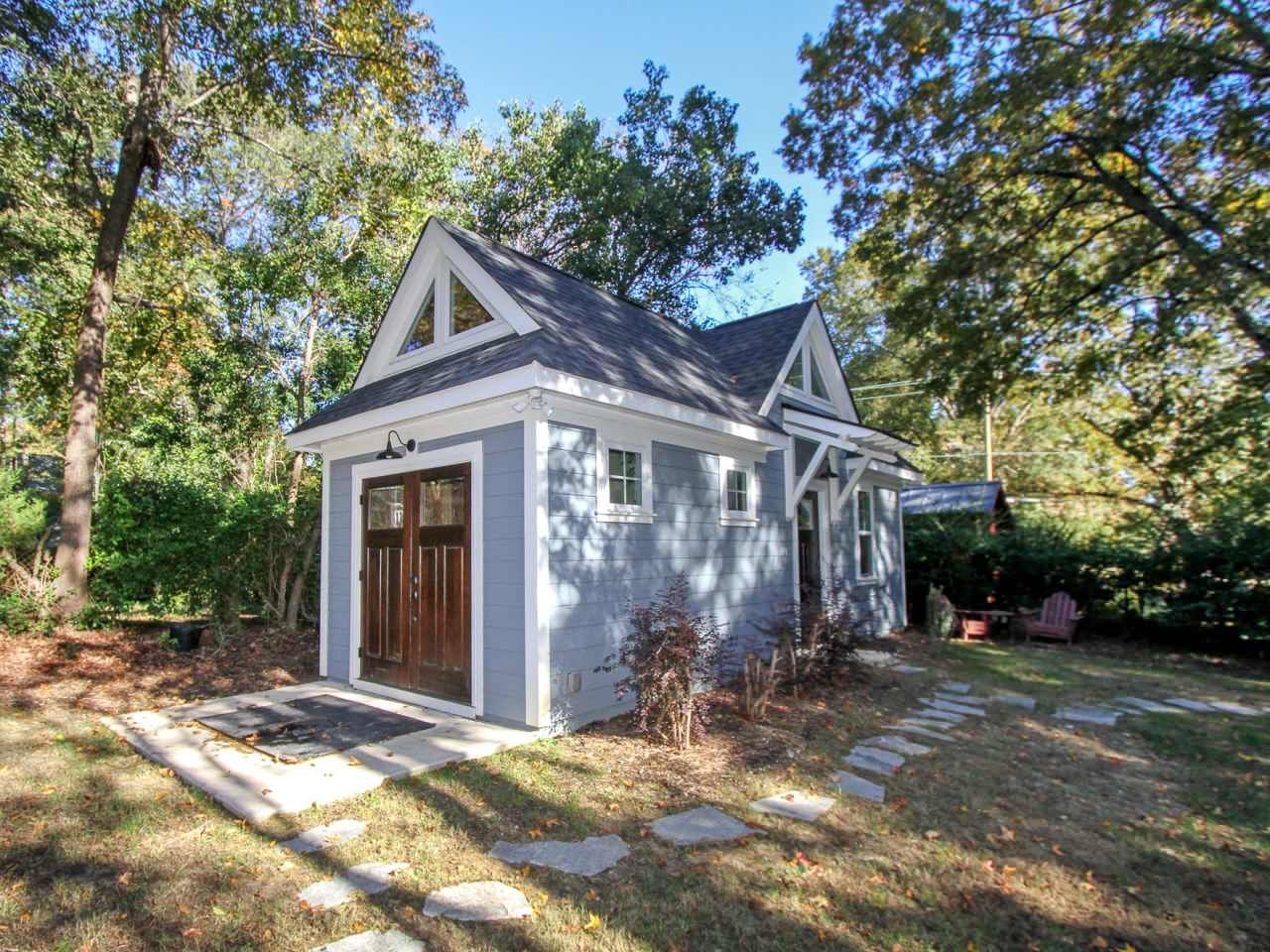 Small blue cottage with a gable roof, brown doors, and stone pathway surrounded by trees.