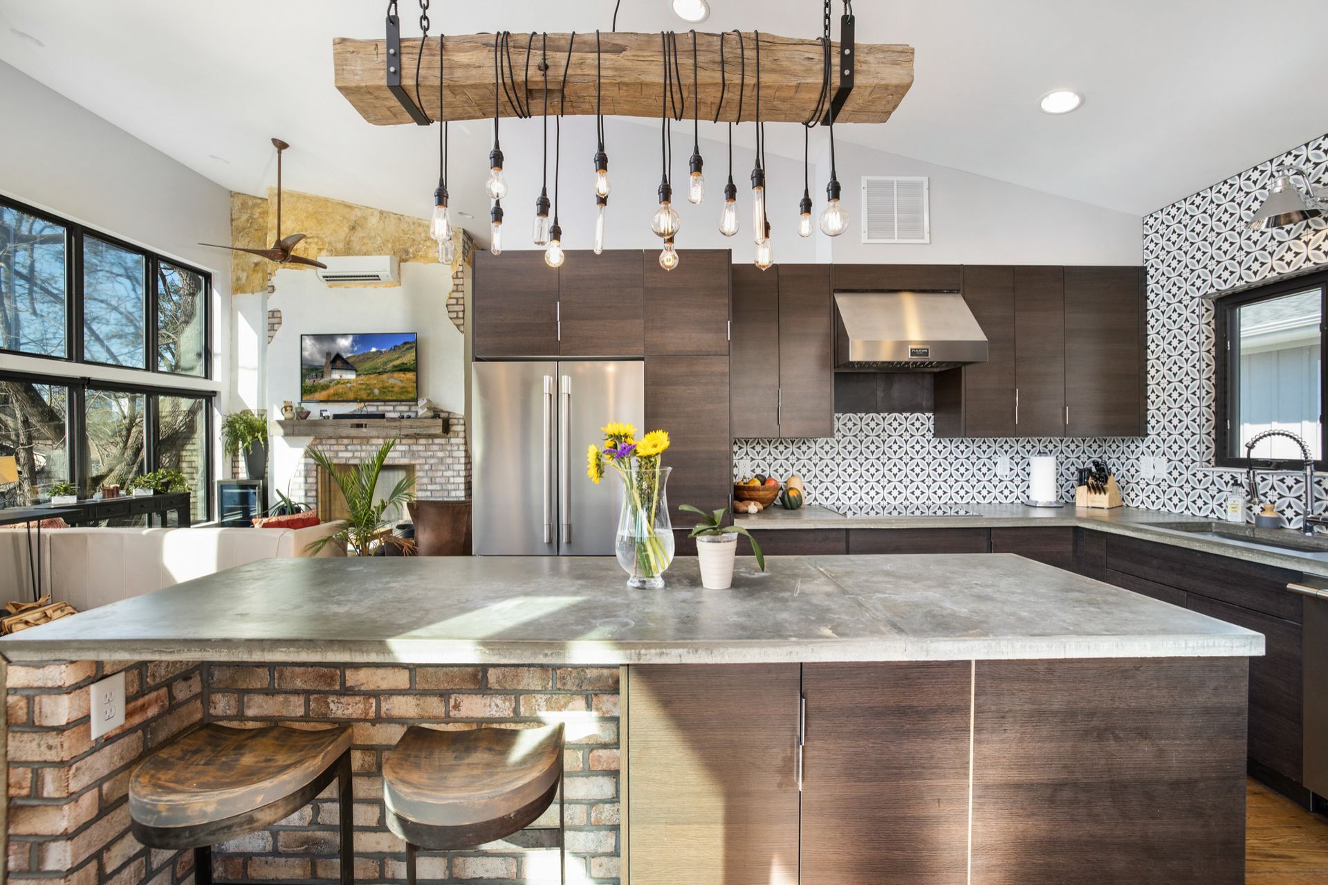 Modern kitchen with large island, brick base, dark cabinets, and a unique light fixture.