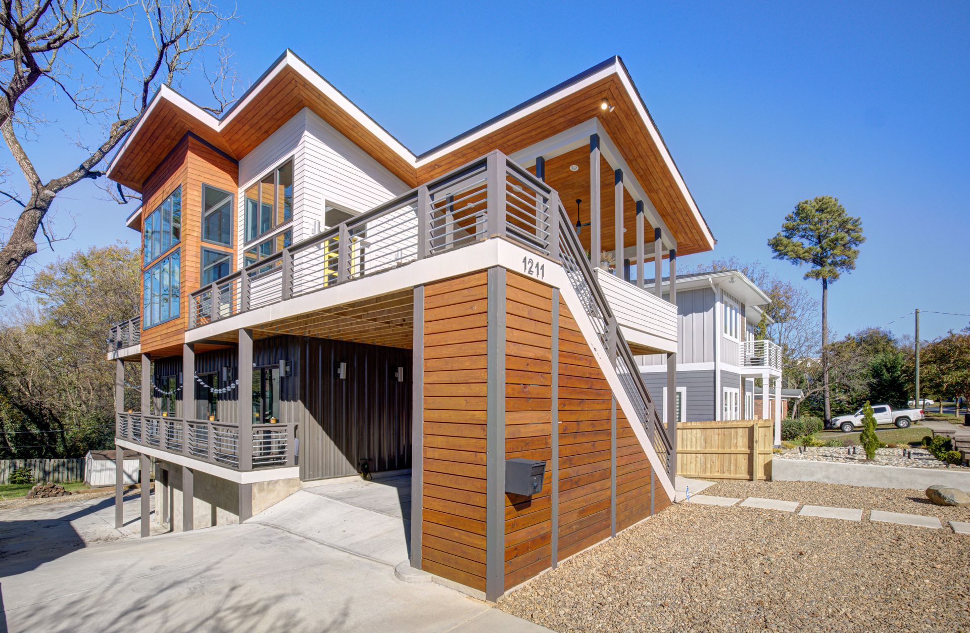 Two-story modern home with a wooden facade and balcony. Gray, white, and wood accents. Sunny outdoor setting.