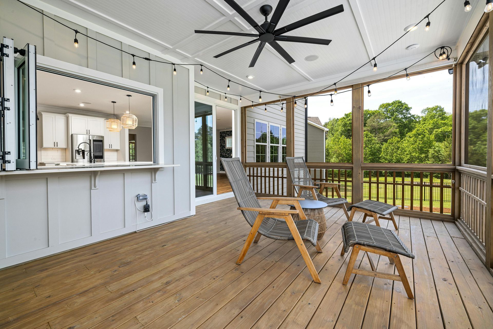 Screened-in porch with seating, a pass-through window to the kitchen, string lights, and a ceiling fan.