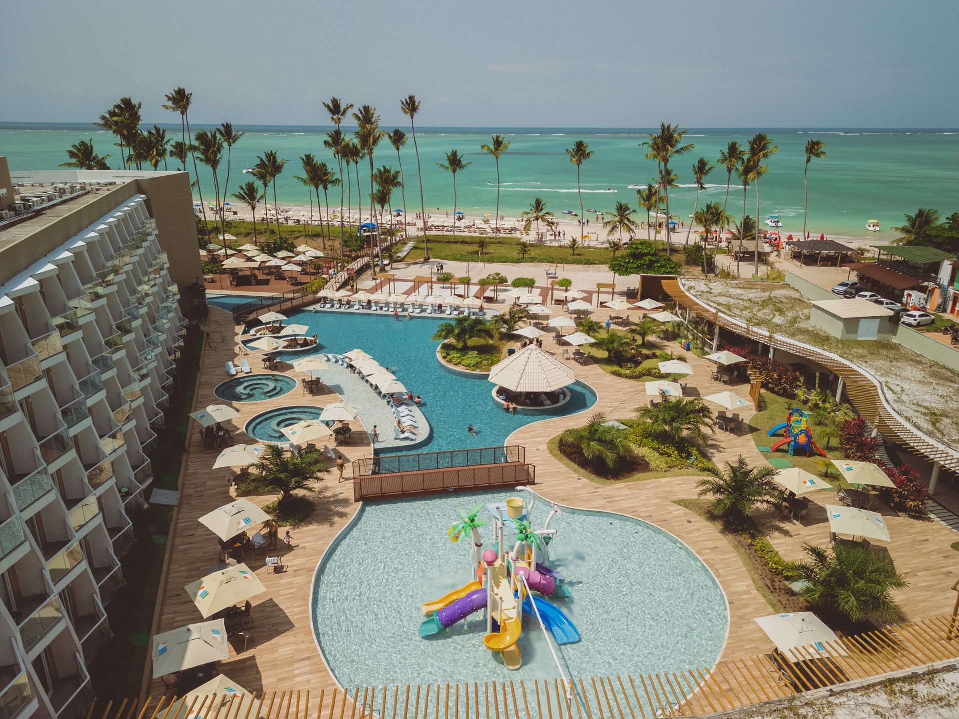 Vista aérea de um resort com piscina, praia e oceano em um ambiente tropical.