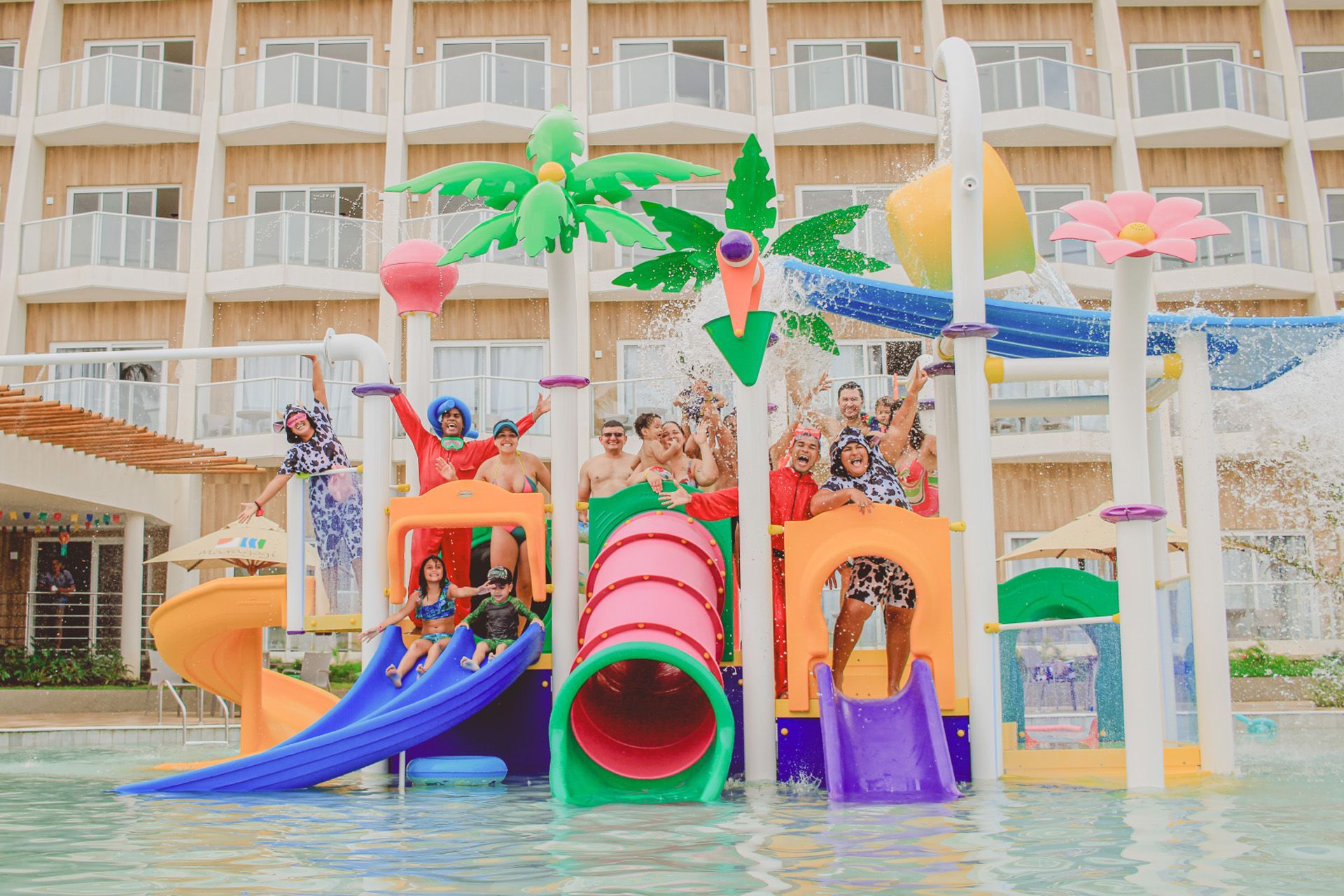 Estrutura colorida de parque aquático em uma piscina de um resort, com um hotel ao fundo sob um céu claro.