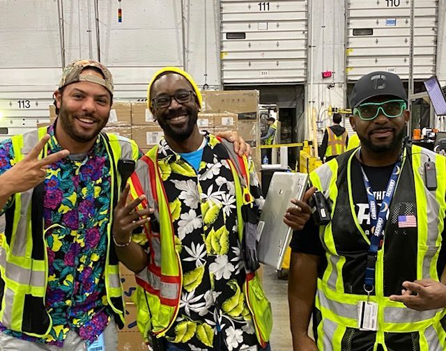 Three men are posing for a picture in a warehouse.