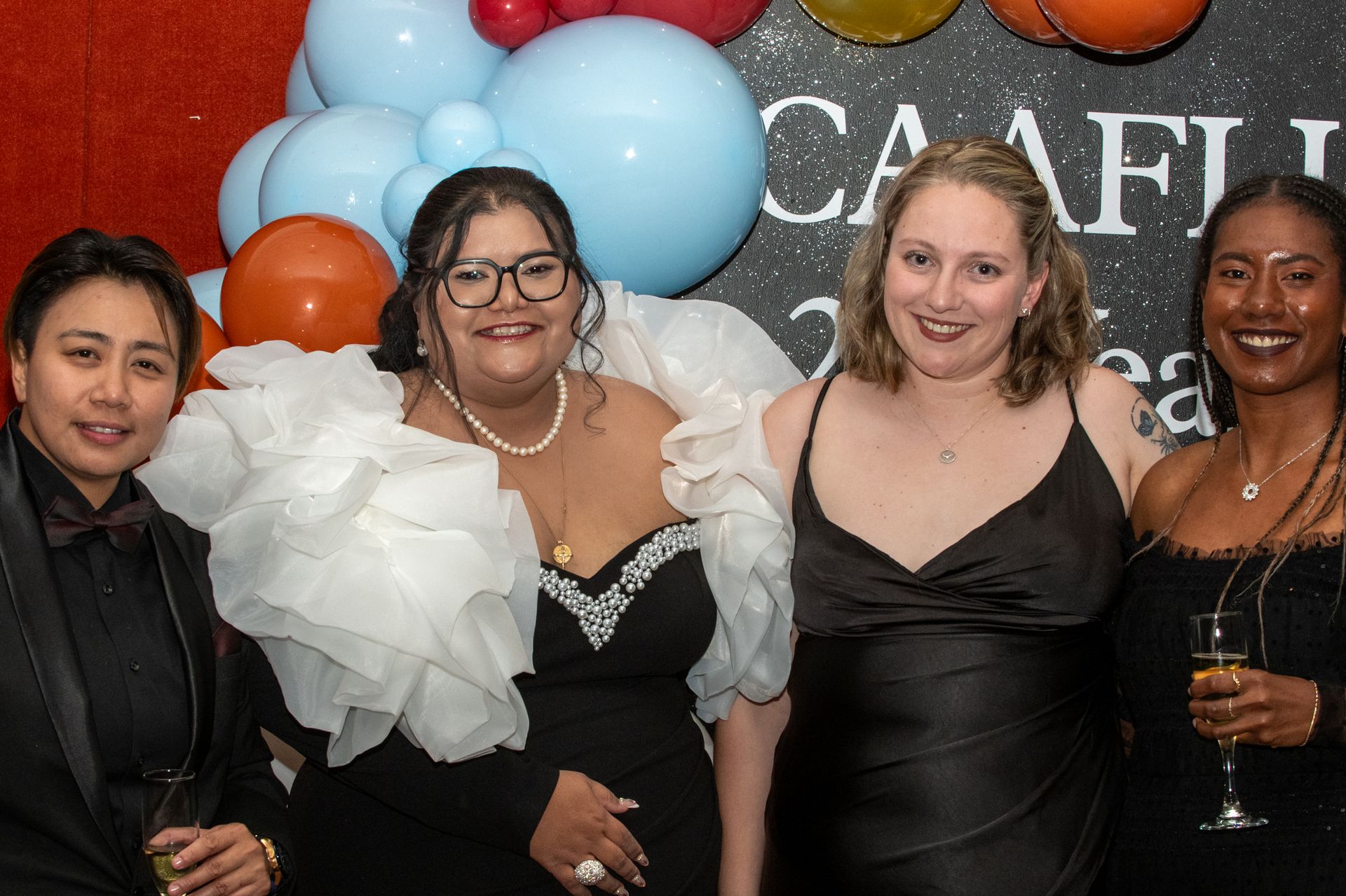 Four women smiling, posing in formal attire, balloons in background. CAAFLU