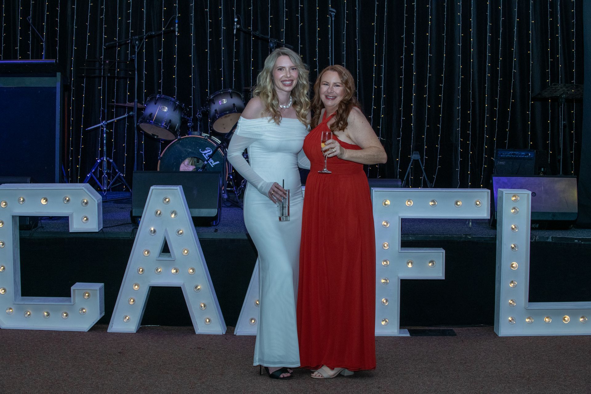 Two women in formal gowns stand near illuminated 