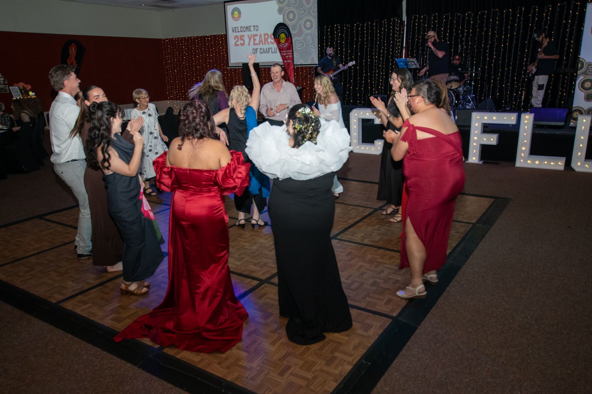CAAFLU People dancing on a lit dance floor at an event. Stage with band and lights in the background.